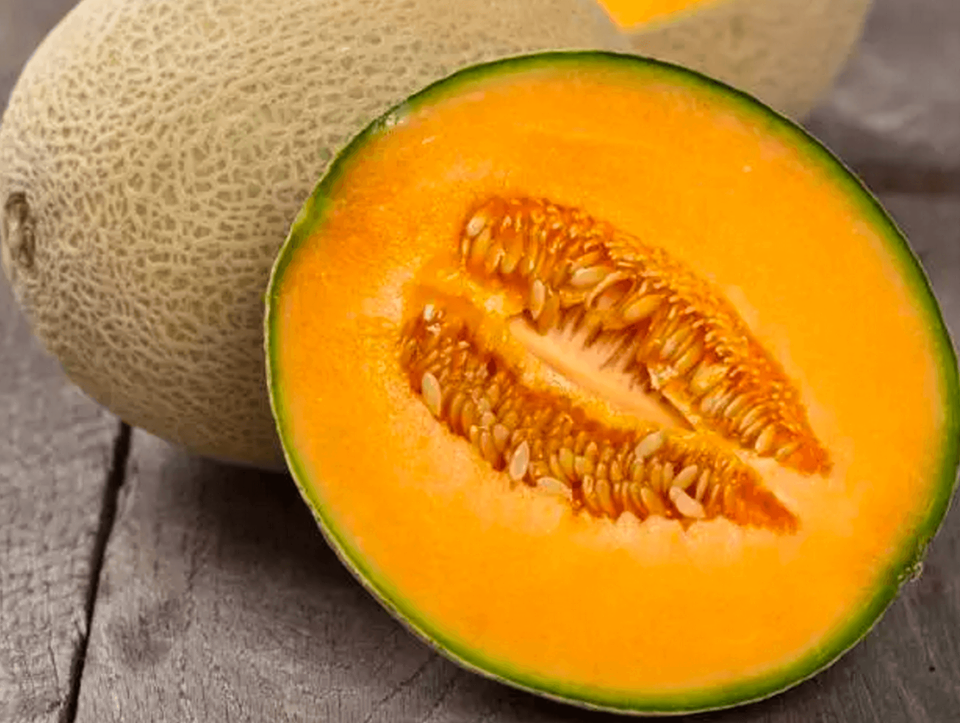 Fresh cantaloupe melon cut in half, showcasing its vibrant orange flesh and seeds, with a whole melon in the background on a wooden surface.
