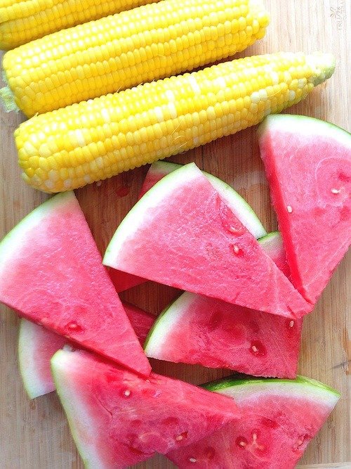Freshly sliced watermelon and yellow corn on a wooden cutting board, showcasing vibrant colors and healthy summer snacks. Perfect for seasonal dishes and refreshing treats.
