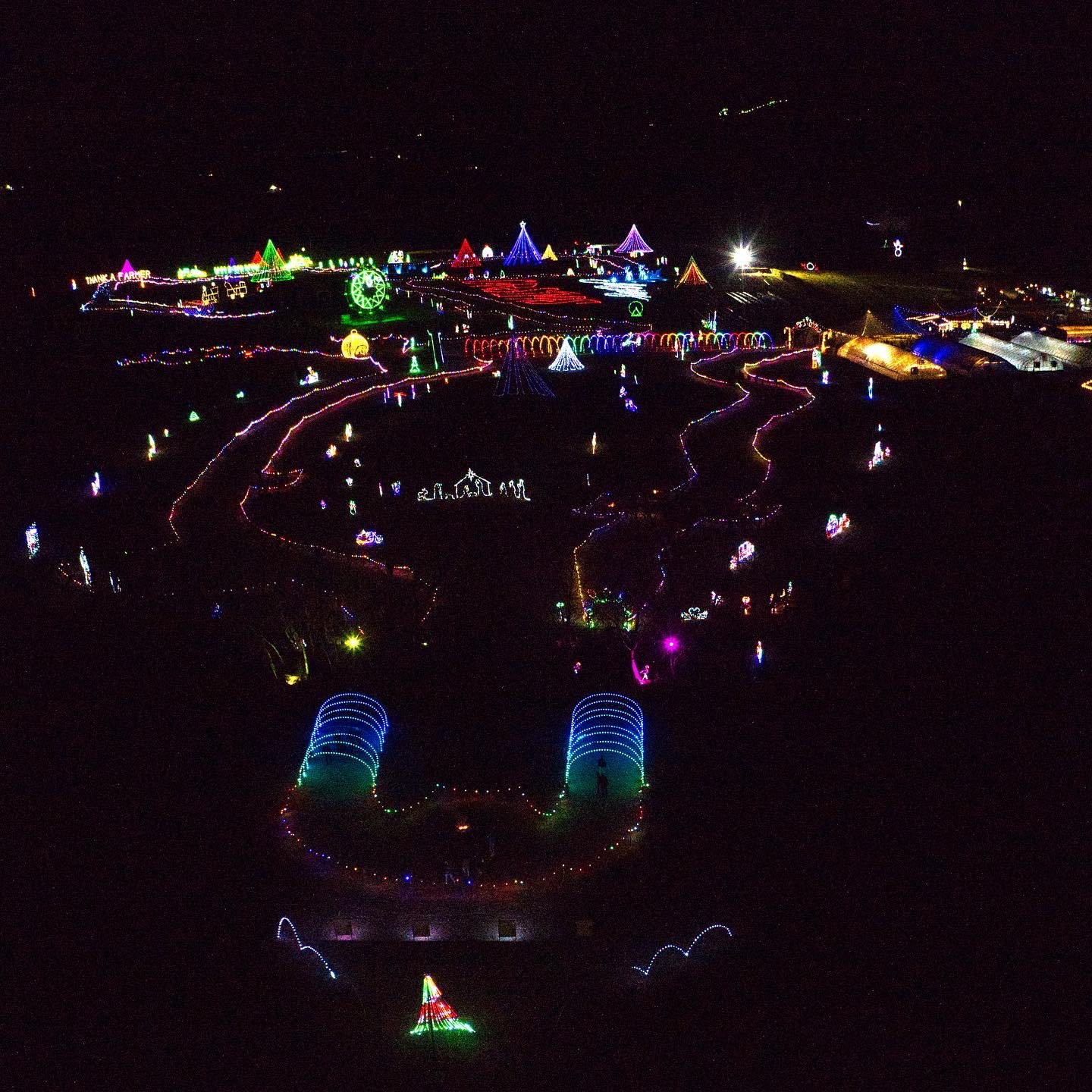 EEE50B10-AC67-43E4-8AB3-18959FED410F Aerial view of a vibrant holiday light display featuring colorful illuminated structures, pathways, and festive decorations in a nighttime setting. The scene showcases various shapes and patterns, creating a magical atmosphere for visitors.