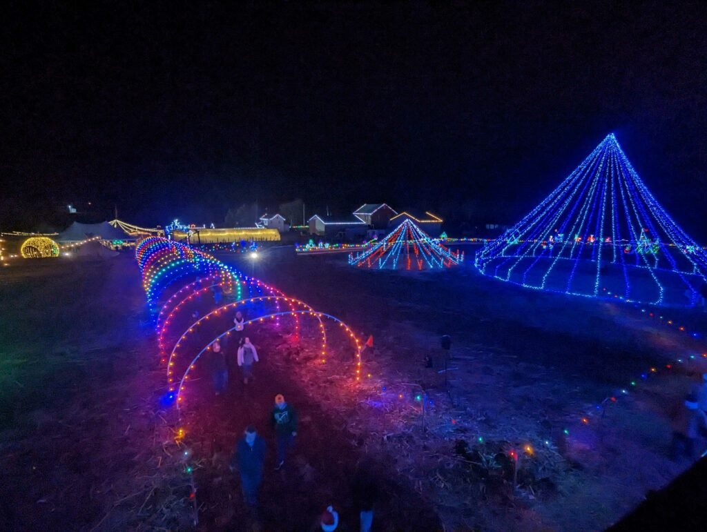 Festive+Light+Display+PA Colorful holiday light display featuring illuminated arches and geometric shapes in a festive outdoor setting at night, with visitors walking through the vibrant pathways.