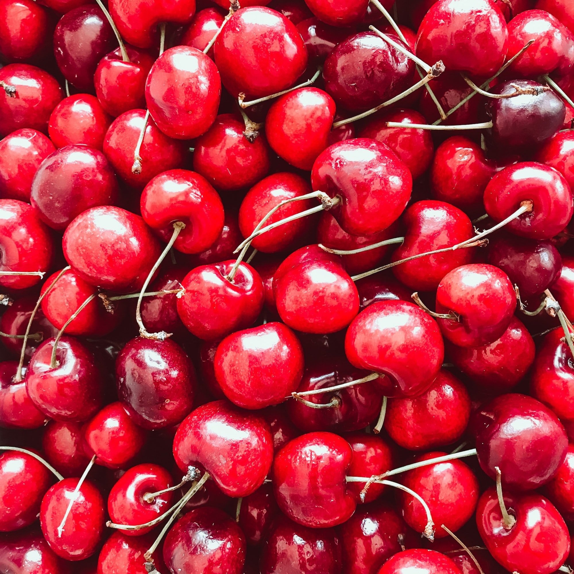 unsplash-image-lFo7eFwr8Fs Fresh, vibrant cherries piled together, showcasing their glossy red skin and green stems, ideal for desserts, snacks, or healthy recipes.